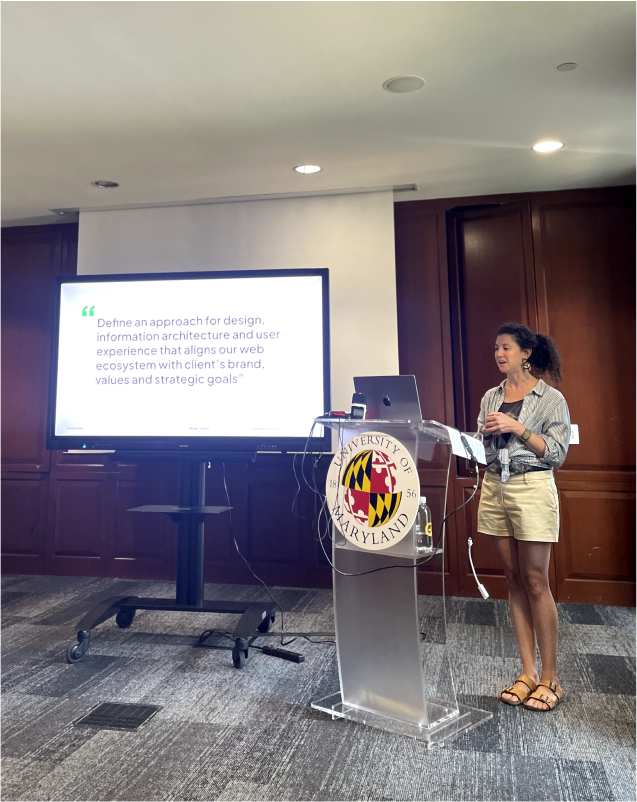 Adrienne speaking in front of a podium with a slides screen